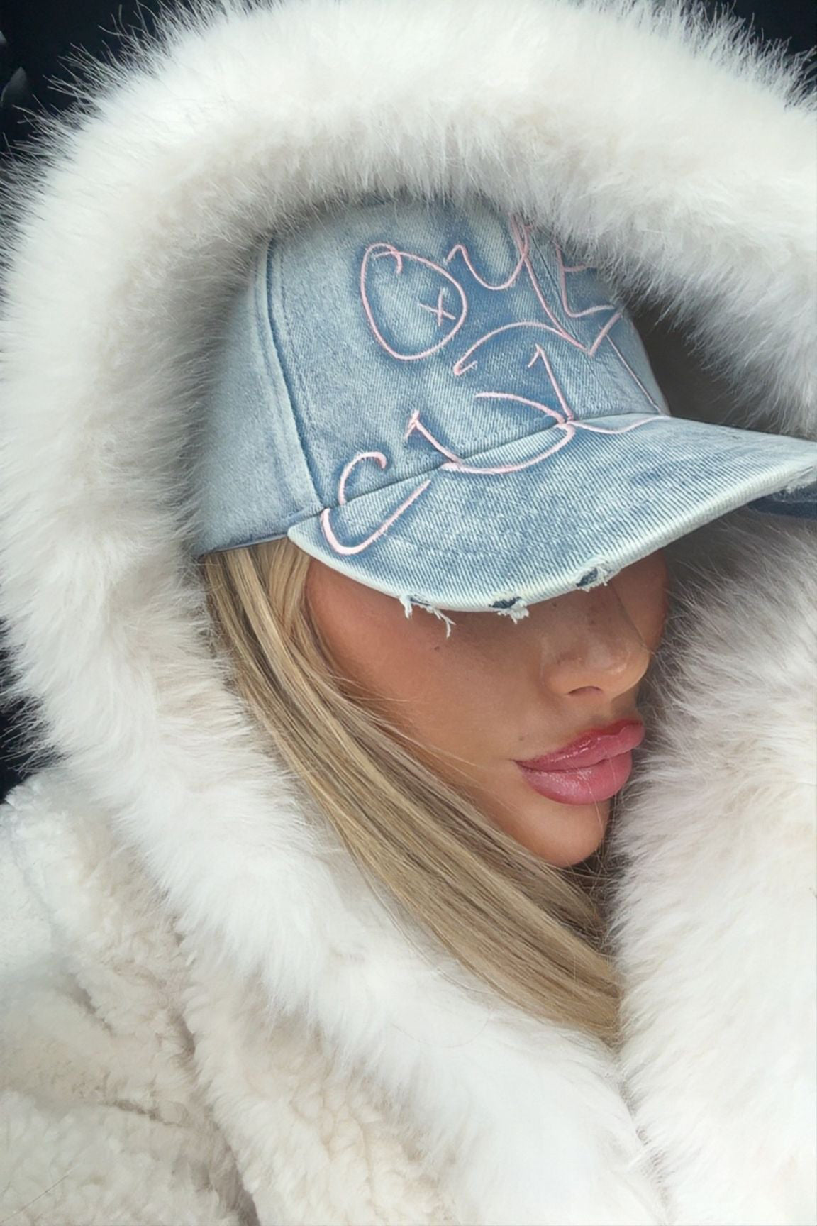 Person wearing a denim cap with white fur trim and a white coat.