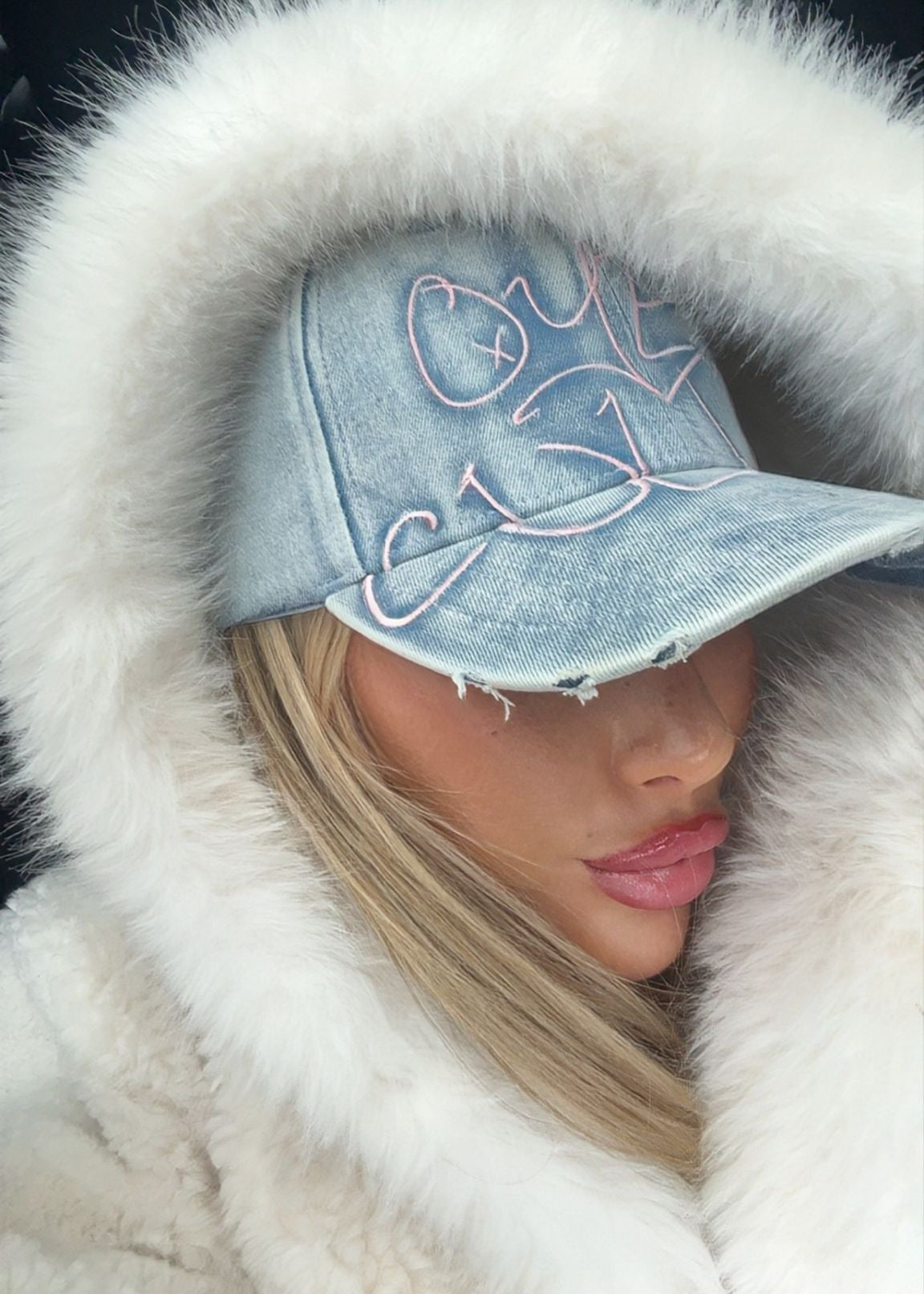 Person wearing a denim cap with white fur trim and a white coat.