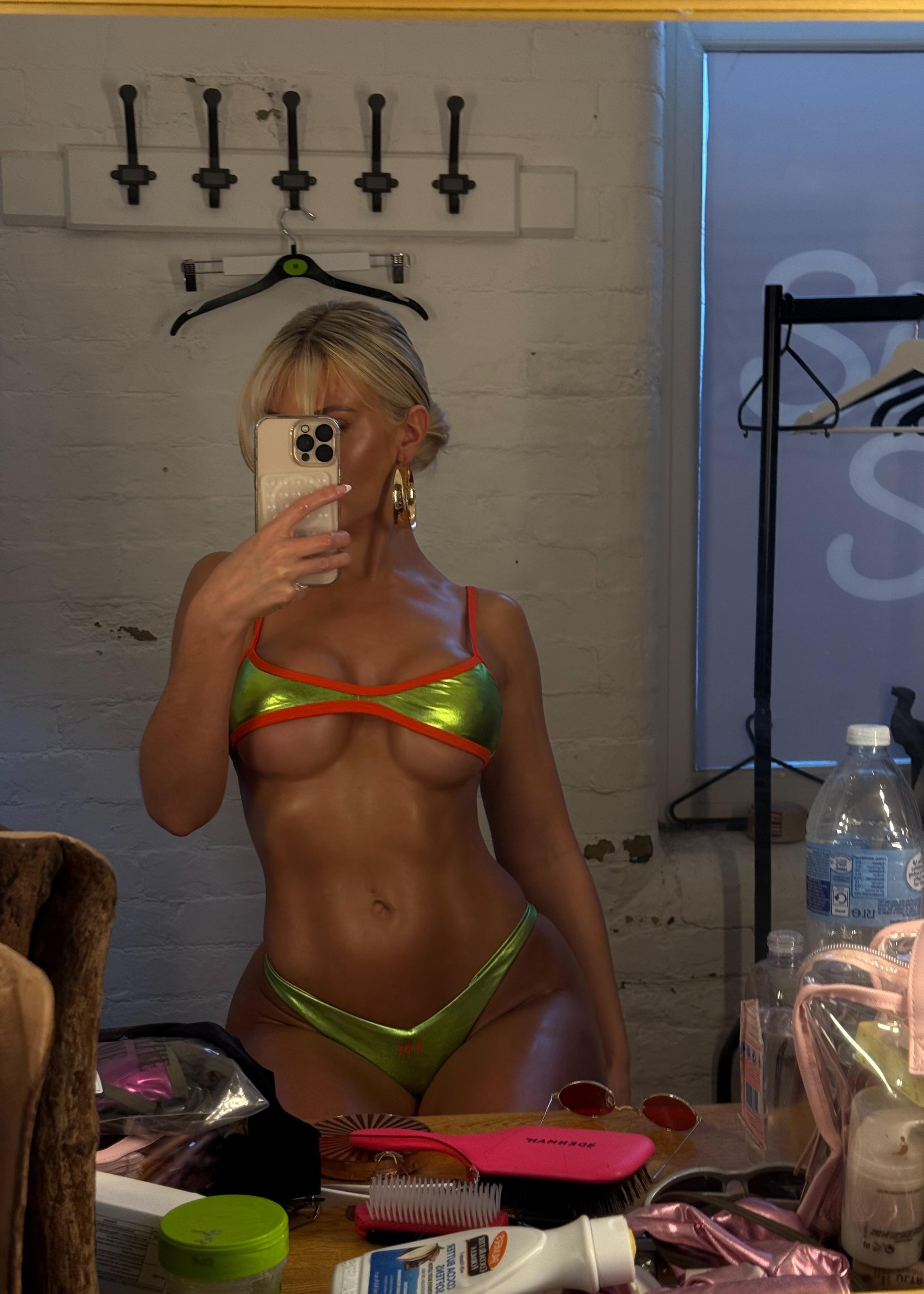 Person taking a mirror selfie wearing a colorful bikini in a room with various items on a table.