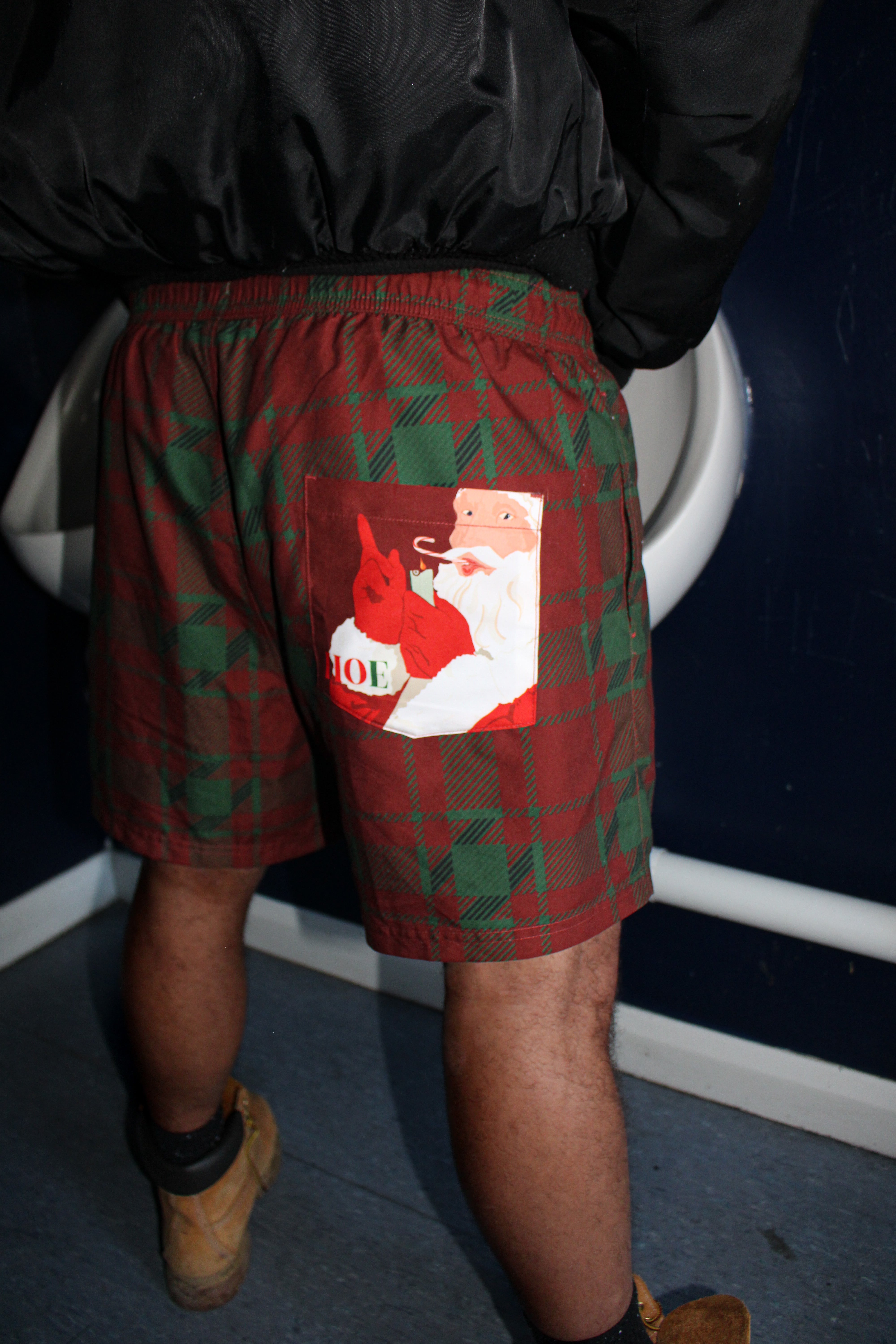 Person wearing red plaid shorts with a Santa Claus graphic in a bathroom.