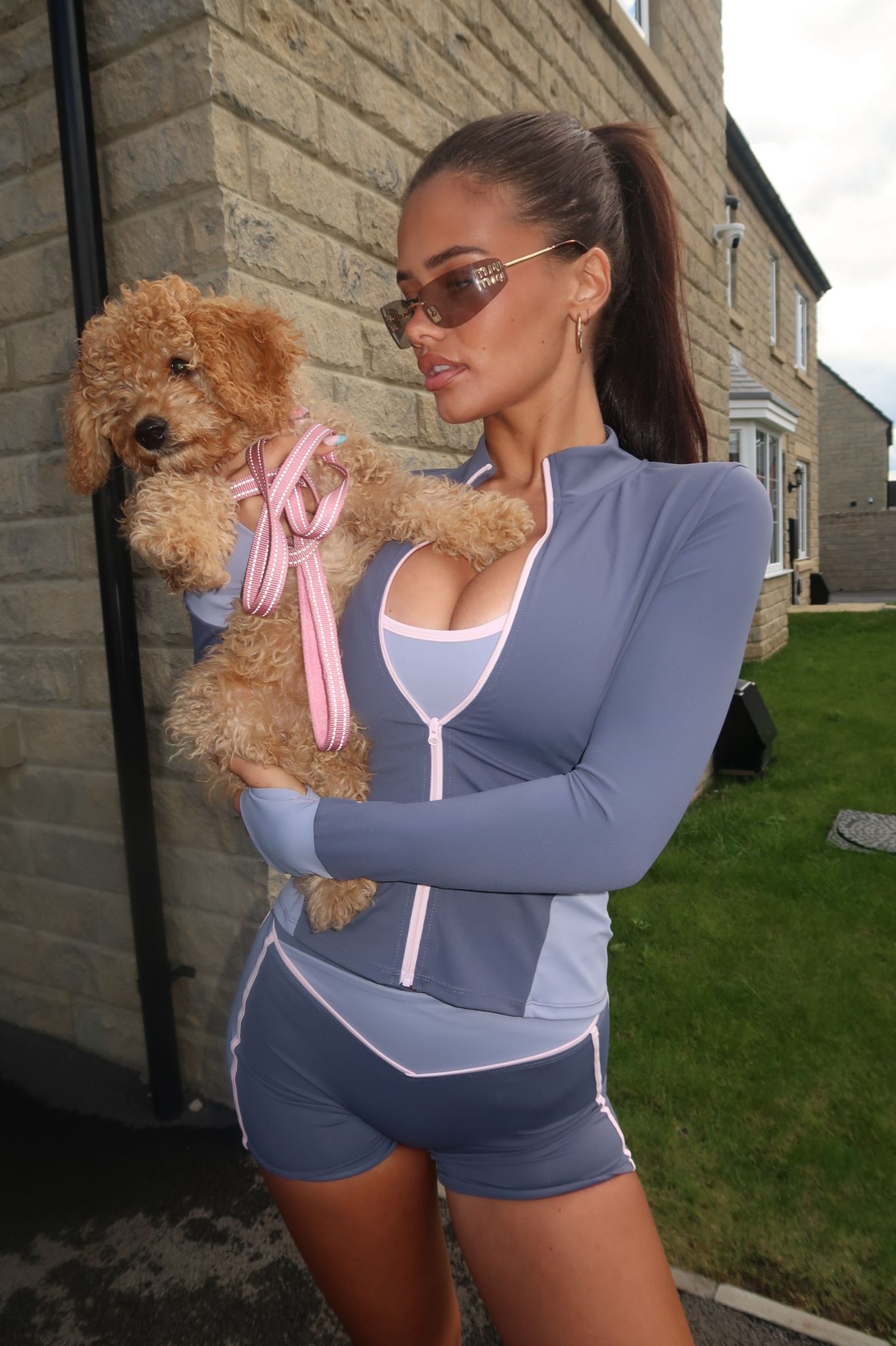 Woman in athletic wear holding a dog with a pink ribbon outdoors.